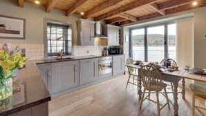 A kitchen with wooden beams, a dining area with a table and chairs, and a view of a lake. - 2 Bed in Inverness (oc-ca324) (Inverness)