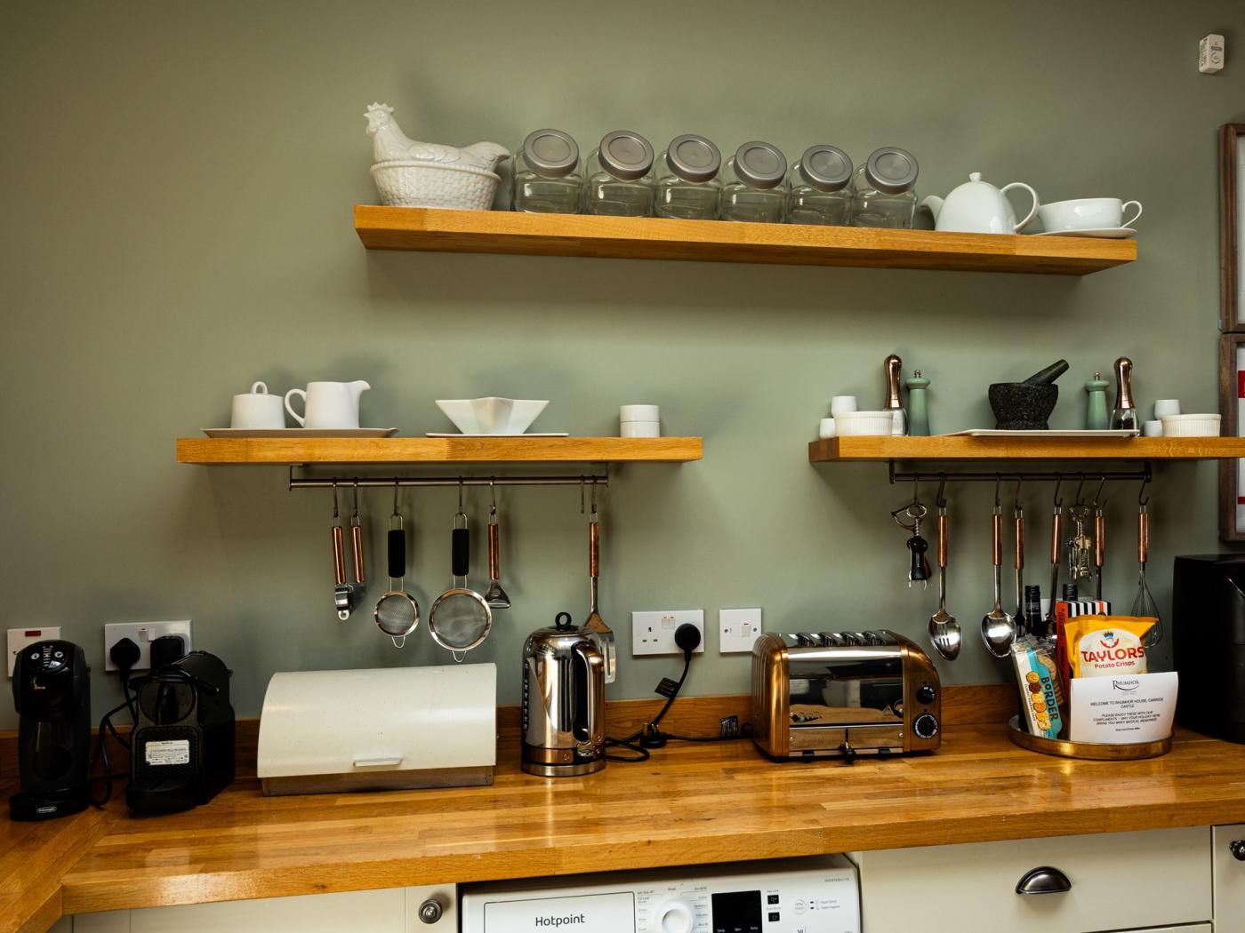 A kitchen with wooden shelves holding kitchenware, a coffee maker, a toaster, and a kettle.