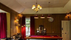 A billiards room with a pool table, a clock, and a leather sofa.