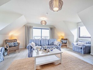 A spacious loft bedroom with a large window, a white ceiling, and a striped sofa set. - 4 Bed in Isle Of Arran (oc-n42556) (Whiting Bay)