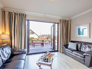 A living room with a sofa, a coffee table, and a view of an outdoor patio with a table and chairs. - 4 Bed in Isle Of Arran (oc-n42556) (Whiting Bay)