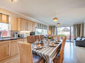 A modern kitchen with wooden cabinets, a dining area with striped tablecloths, wicker chairs, and a view of the outdoors. - 4 Bed in Isle Of Arran (oc-n42556) (Whiting Bay)