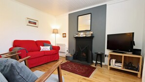 A living room with a red sofa, a grey armchair, a fireplace, a television, and a bookshelf. - 3 Bed in Isle Of Skye (oc-ca298) (Uig)