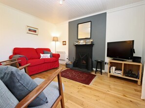 A living room with a red sofa, a grey armchair, a fireplace, a television, and a bookshelf. - 3 Bed in Isle Of Skye (oc-ca298) (Uig)