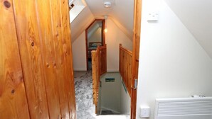 A narrow hallway with wooden walls and a sloped ceiling, leading to a bedroom with a bed and a window. - 3 Bed in Isle Of Skye (oc-ca298) (Uig)