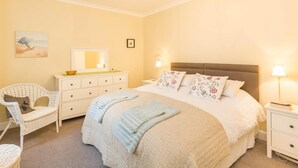 Une chambre à coucher comprenant un lit, des tables de chevet, une chaise, une commode, un lustre et des œuvres d’art murales.