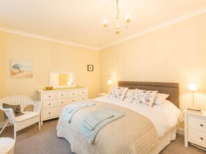 A bedroom with a bed, bedside tables, a chair, a dresser, a chandelier, and wall art. - 4 Bed in Isle Of Arran (oc-ca381) (Brodick)