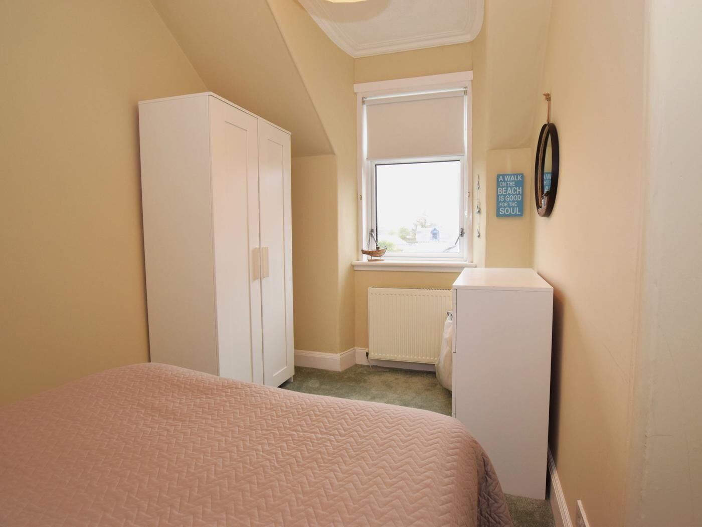 A bedroom with a bed, a wardrobe, a radiator, a window with a view, and a wall clock.