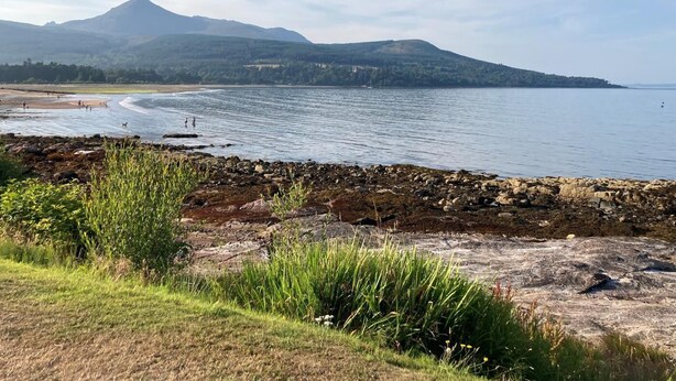 Un paysage côtier avec une rive rocheuse, une plage et des montagnes à l’horizon.