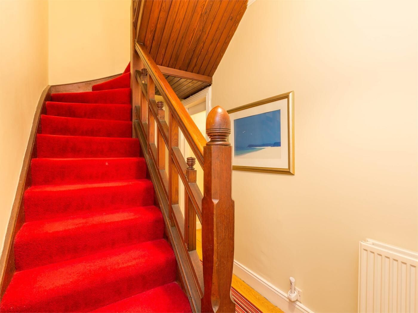 A staircase with red carpet, wooden handrail, and a framed picture on the wall.