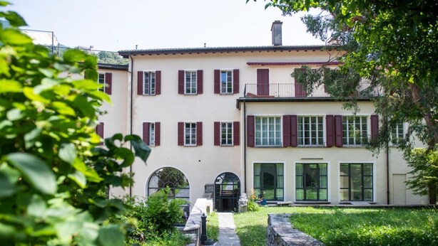 A two-story building with a stone pathway leading to the entrance, surrounded by greenery. - Garden, Castel x6PAX (Bellinzona)