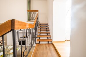 A staircase with wooden steps and a metal railing, leading to a room with a white wall and a window.