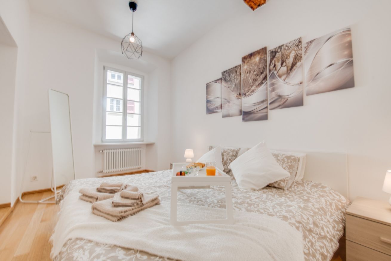 Une chambre à coucher avec un lit, une table de chevet avec une lampe, une fenêtre et des œuvres d’art accrochées au mur.