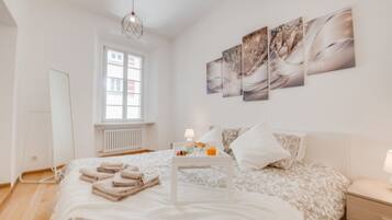 Une chambre à coucher avec un lit, une table de chevet avec une lampe, une fenêtre et des œuvres d’art accrochées au mur.