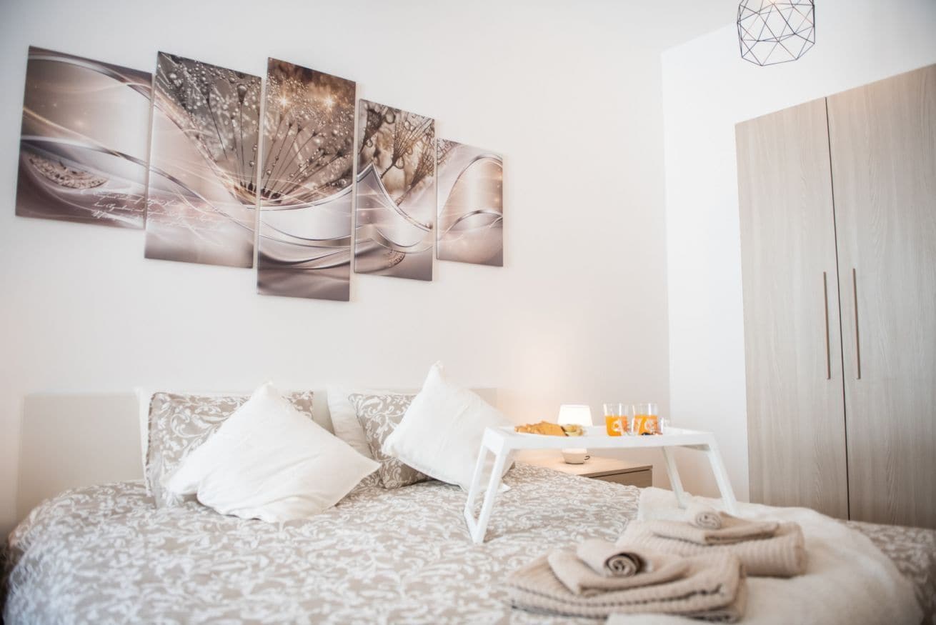 Une chambre à coucher avec un lit, des oreillers, une table de chevet avec une lampe et une boisson orange, et une armoire.