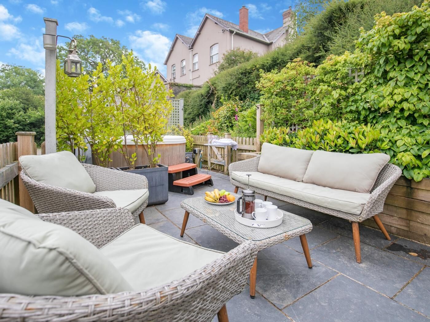 Une terrasse dotée de meubles en osier, d’un jacuzzi et d’une table où sont disposés des fruits et une cafetière.