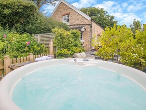 A hot tub in a garden with a stone building in the background. - 2 Bed in Ilfracombe (oc-76407) (Ilfracombe)
