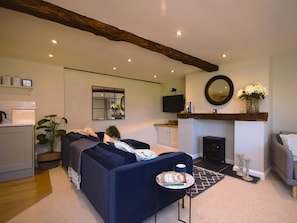 A living room with a dark blue sofa, a small table with a book and a mug, a fireplace, and a television mounted on the wall. - 2 Bed in Ilfracombe (oc-76407) (Ilfracombe)