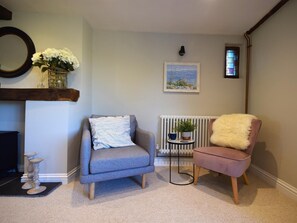 A living room with a grey armchair, a pink chair, a radiator, a small table with a plant, and a framed painting on the wall. - 2 Bed in Ilfracombe (oc-76407) (Ilfracombe)