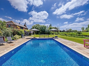A rectangular swimming pool with a tiled edge, surrounded by a patio area with chairs and umbrellas. - 5 Bed in Ashford (oc-76428) (Smarden)