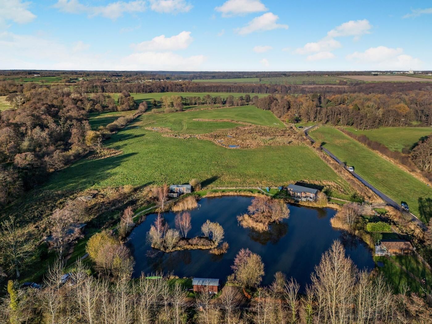 Une vue aérienne d’un paysage rural avec un étang, des champs et quelques bâtiments dispersés.