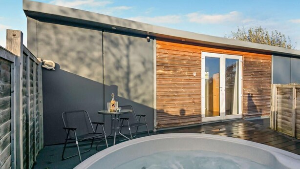 A modern outdoor pool area with a hot tub, a wooden deck, and a small table with chairs. - 1 Bed in Norwich (oc-76493) (East Harling)