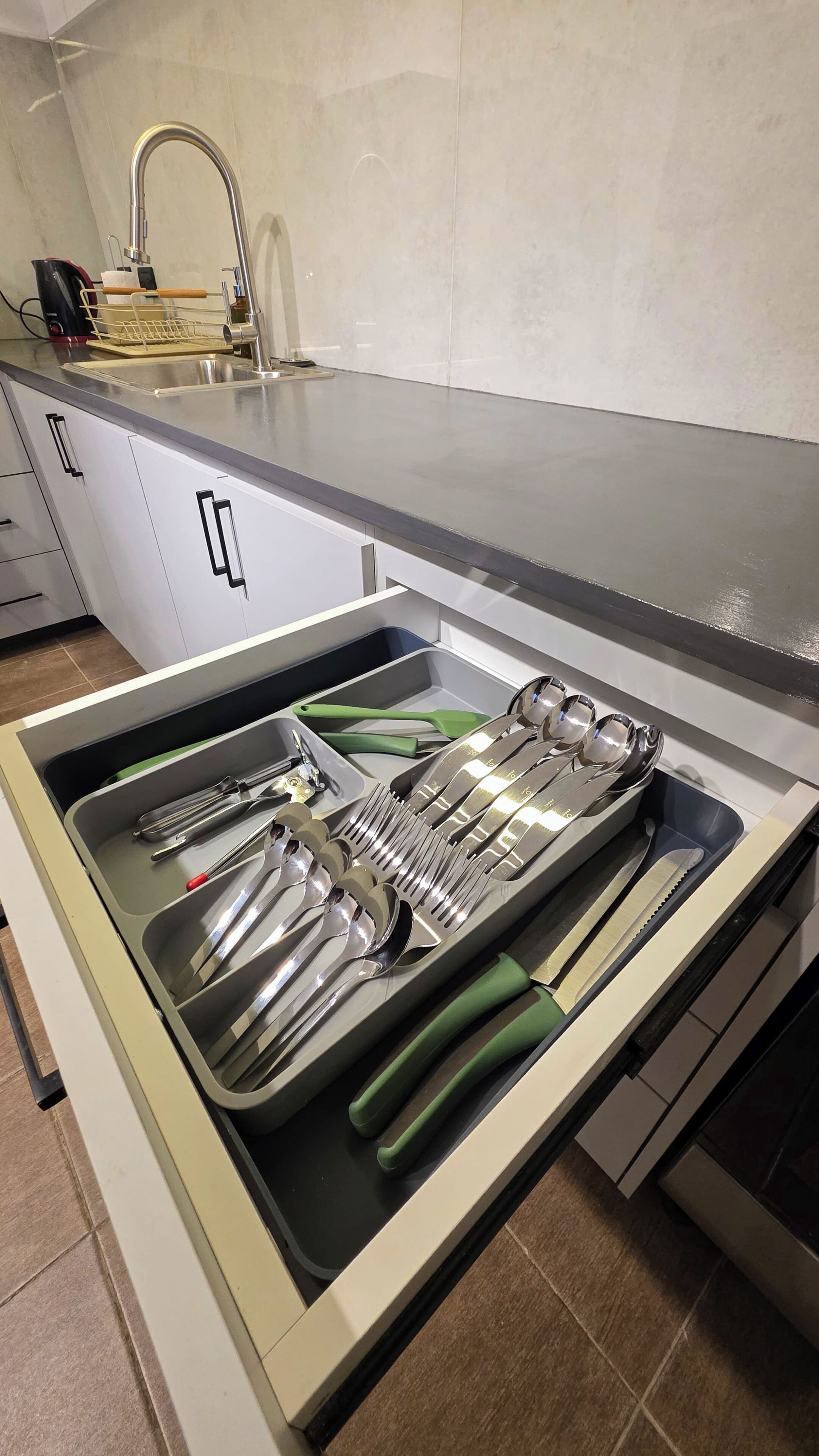 Una cocina con pileta de acero inoxidable, lavavajillas integrado y un cajón con utensilios.