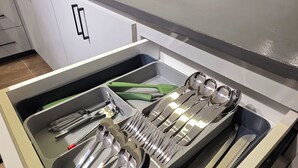 A kitchen with a stainless steel sink, a built-in dishwasher, and a drawer with utensils.