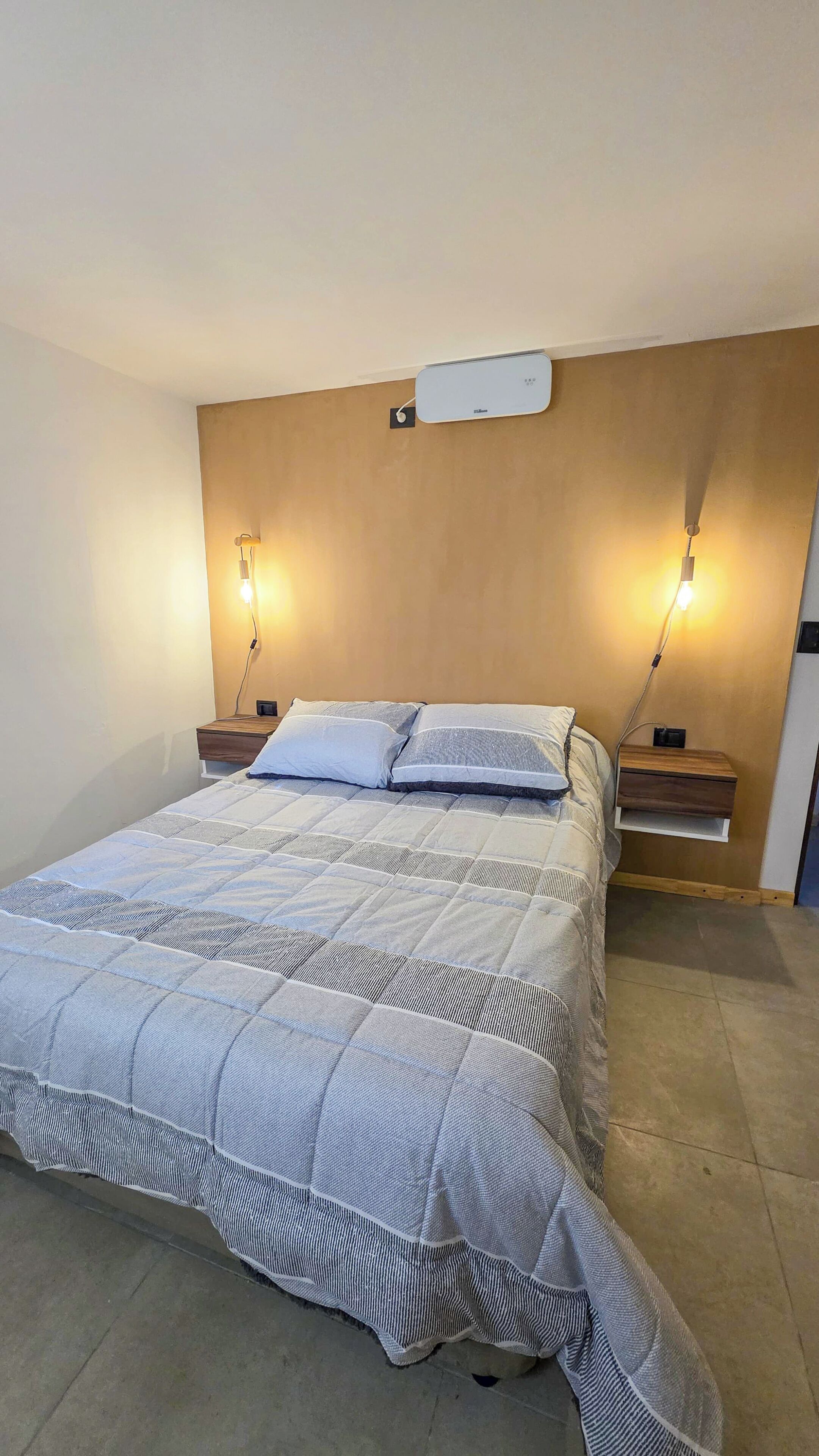 Ein Schlafzimmer mit einem Bett, zwei Nachttischen, einer Wandklimaanlage und zwei Wandleuchten.