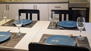 A dining area with a white table set for four, black chairs, and a kitchen in the background.