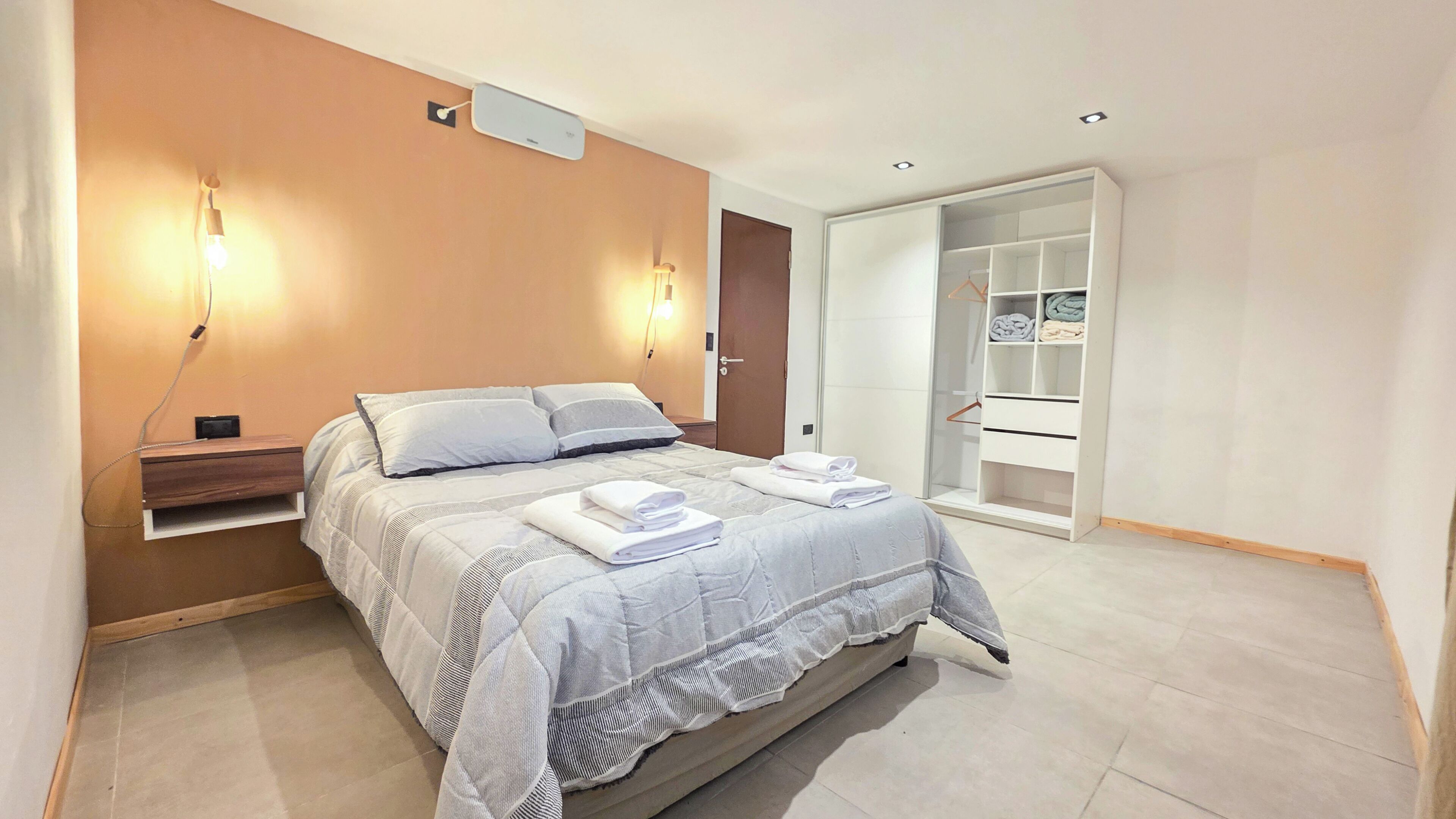 Un dormitorio moderno con cama, mesitas de noche, armario y vestidor.