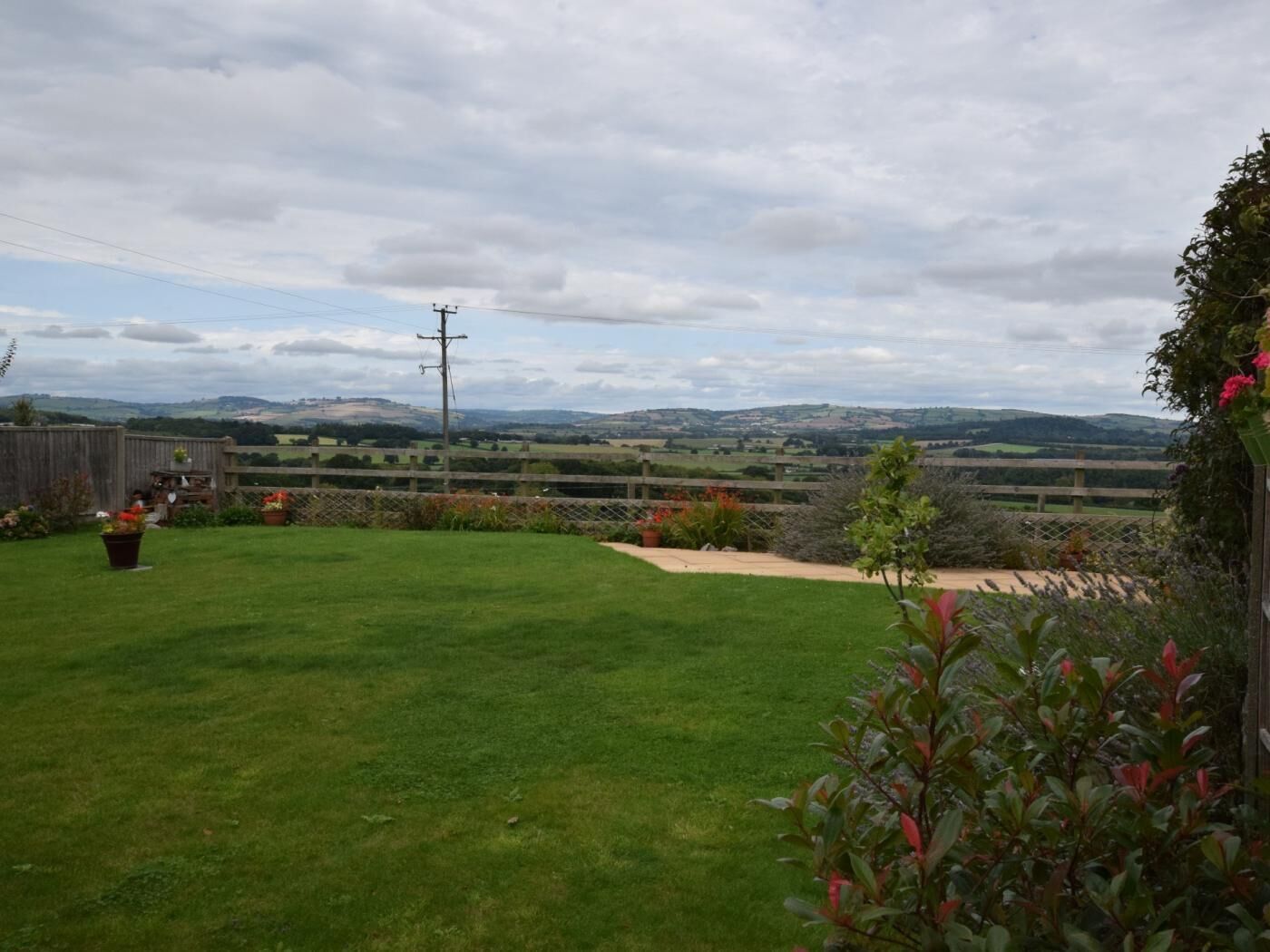 A grassy backyard with a wooden fence, potted plants, and a view of rolling hills in the distance.