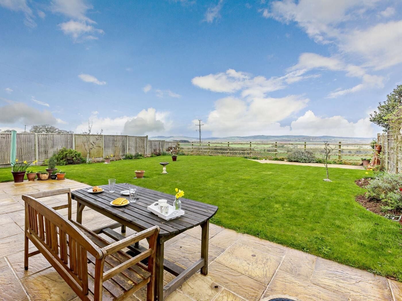 Une terrasse avec une table et des chaises, une pelouse verdoyante et une vue sur la campagne.