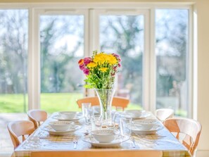 A dining table set for six with a vase of flowers in the center, surrounded by chairs. - 3 Bed in Wareham (oc-76648) (South Trigon)