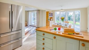 Eine moderne Küche mit einem Edelstahl-Kühlschrank, einer Holzarbeitsplatte und Blick auf den Garten durch große Fenster.