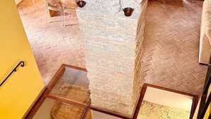 Een kamer met een stenen muur, een houten vloer, een glazen tafel en een klein houten kastje.