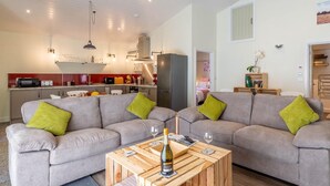 Ein modernes Wohnzimmer mit zwei grauen Sofas, einem Holztisch und einer Küche im Hintergrund.