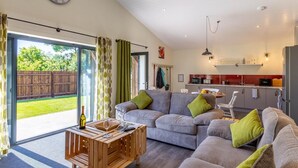 Ein modernes Wohnzimmer mit einer Sofagarnitur, einem Holztisch und einem Essbereich, mit einer Küche im Hintergrund.
