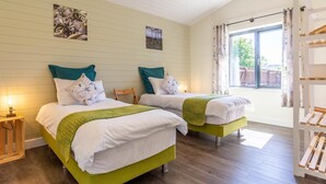 Ein Zimmer mit zwei Betten, Holzboden, einem Fenster mit Blick und einem Regal mit Gegenständen.