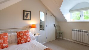 Un dormitorio con cama, mesita de noche, lámpara, silla, radiador, ventana y puerta.