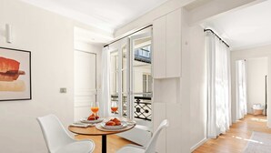 A dining area with a table, two chairs, and a window with curtains. - Charming 1BR Sleeps 4 - Montorgueil (Paris)