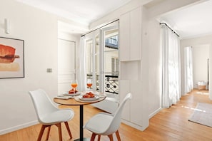 A dining area with a table, two chairs, and a window with curtains. - Charming 1BR Sleeps 4 - Montorgueil (Paris)