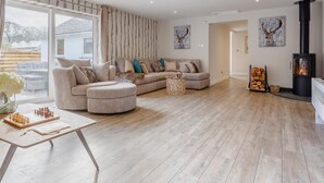 Un salon spacieux avec un grand canapé, une table basse, une cheminée et une vue dégagée sur l’extérieur, accessible par une porte coulissante.