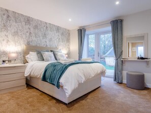 A bedroom with a bed, bedside tables, a nightstand, a mirror, and a view of the outside. - 6 Bed in Penzance (oc-77228) (Relubbus)