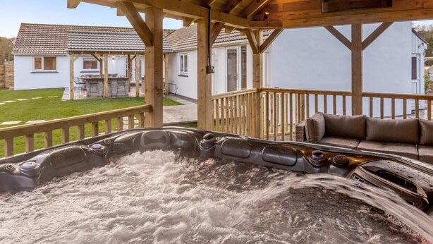 Un bain à remous sous une pergola en bois, avec vue sur une maison et un jardin.