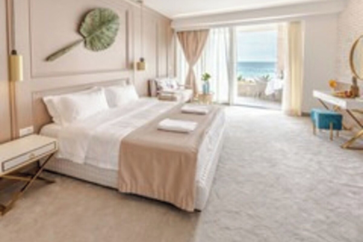 Habitación de hotel con cama, mesita de noche, lámpara y vista al mar.