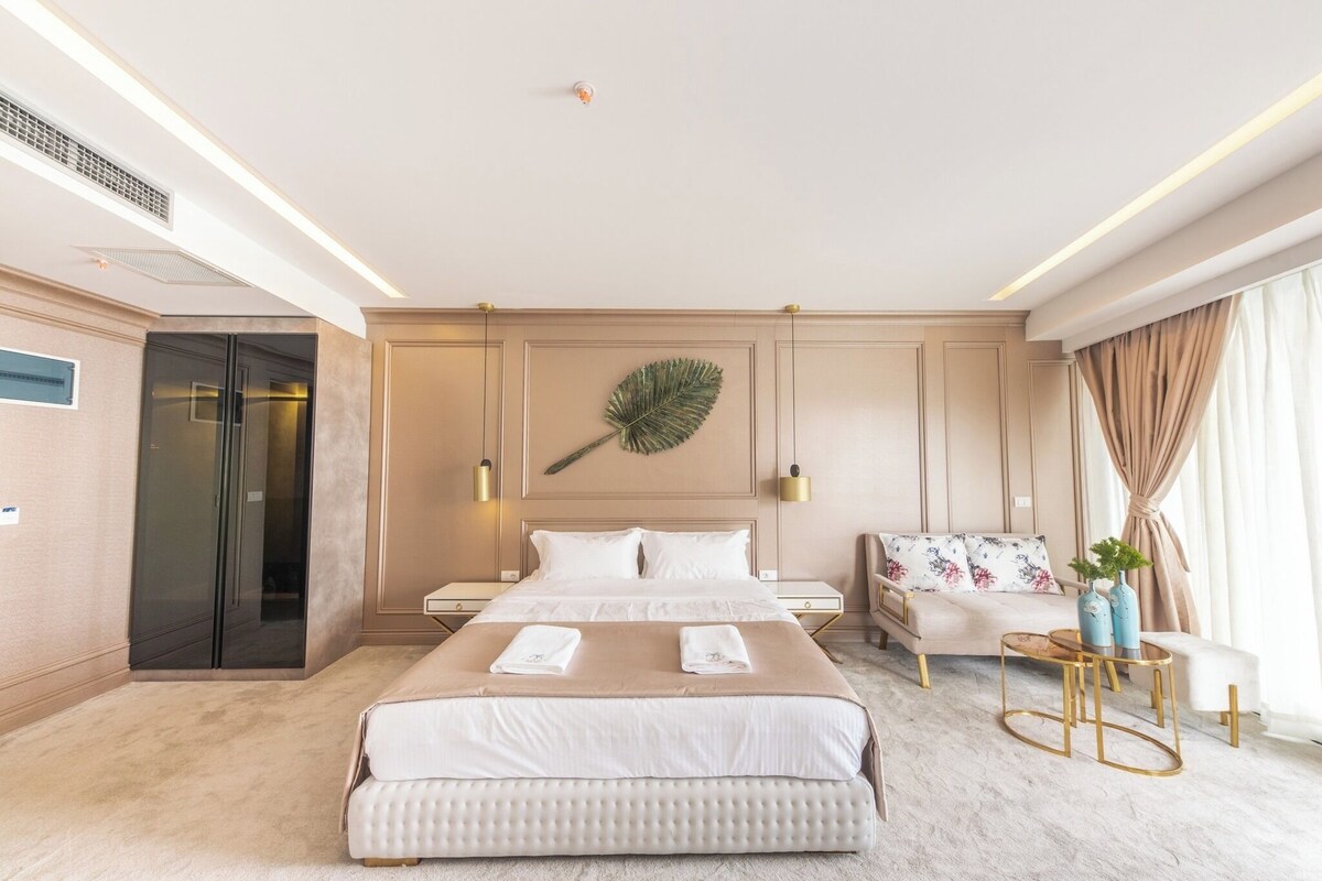 Una habitación de hotel con una cama grande, un sofá, una mesita y una hoja decorativa en la pared.
