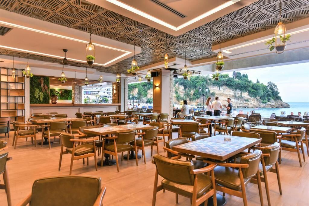 A restaurant with wooden tables and chairs, hanging plants, and a view of the sea.
