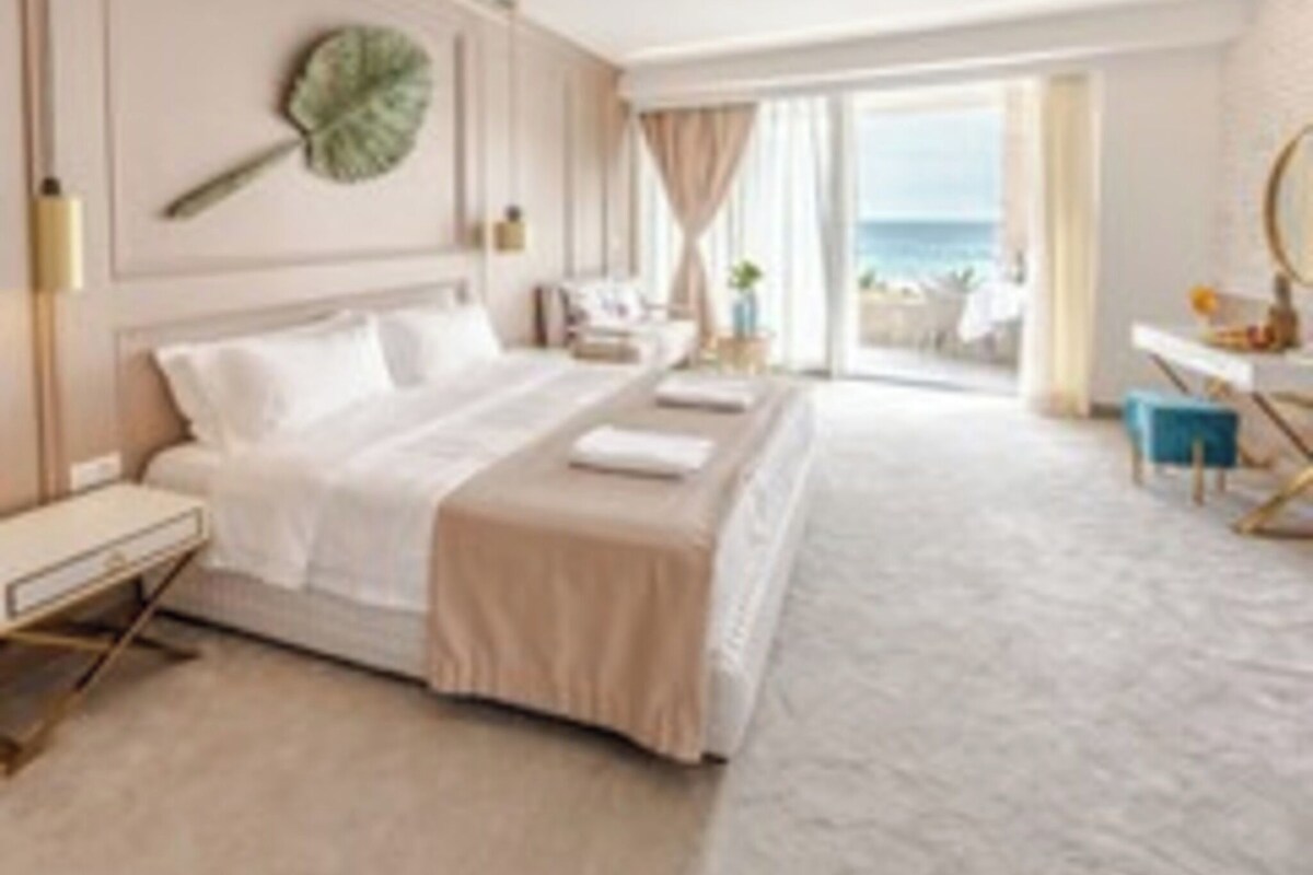 Habitación de hotel con cama, mesita de noche, lámpara y vista al mar.