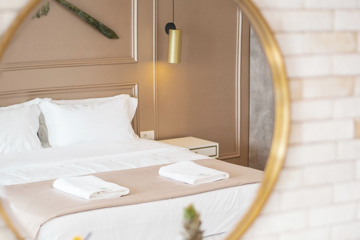 A hotel room with a bed, a round mirror, and a fruit bowl on the side.